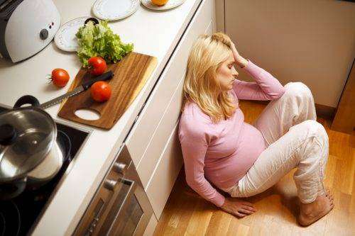 Young lonely pregnant women sitting on the kitchen floor.